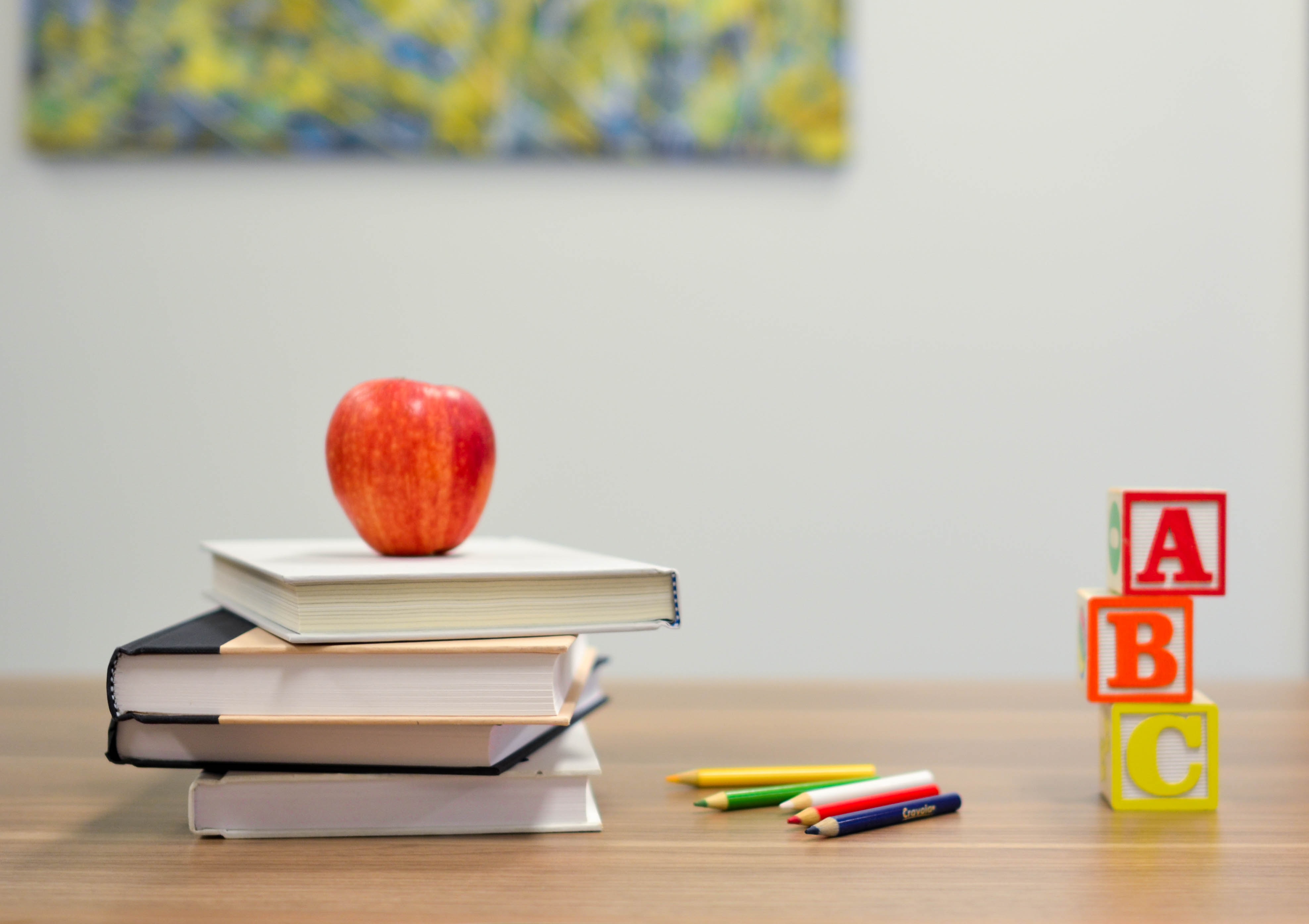 Image of red apple on top of 4 stacked books on classroom desk
